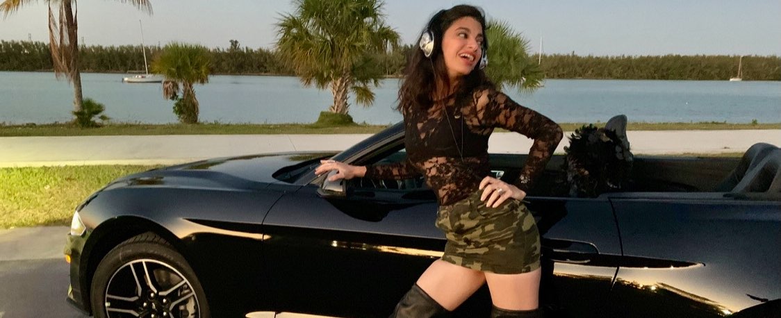 Viviam Maria Lopez wearing headphones and smiling in front of a black car by the bay of Key Biscayne